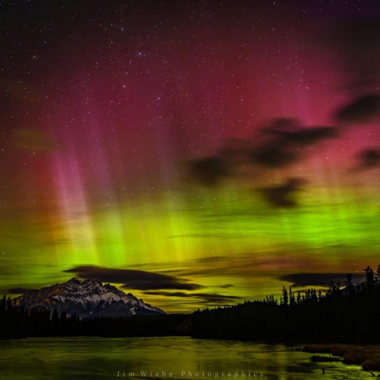 Green and pink aurora borealis over a mountain lake near Canmore, Alberta
